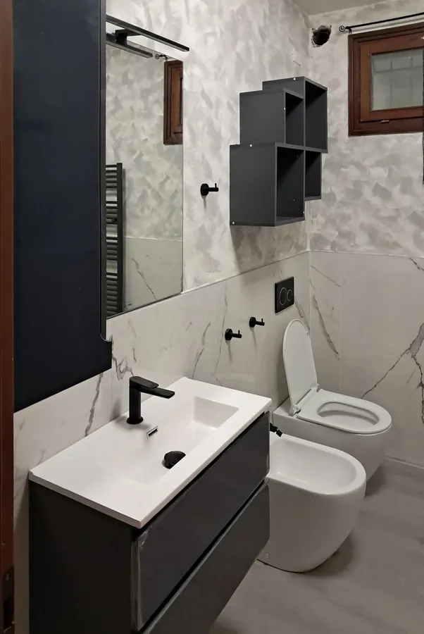Bagno con mobile antracite, rubinetteria nera e pareti effetto marmo