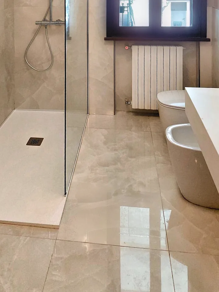 Dopo: lo stesso bagno con doccia in vetro, rivestimento effetto marmo e sanitari nuovi