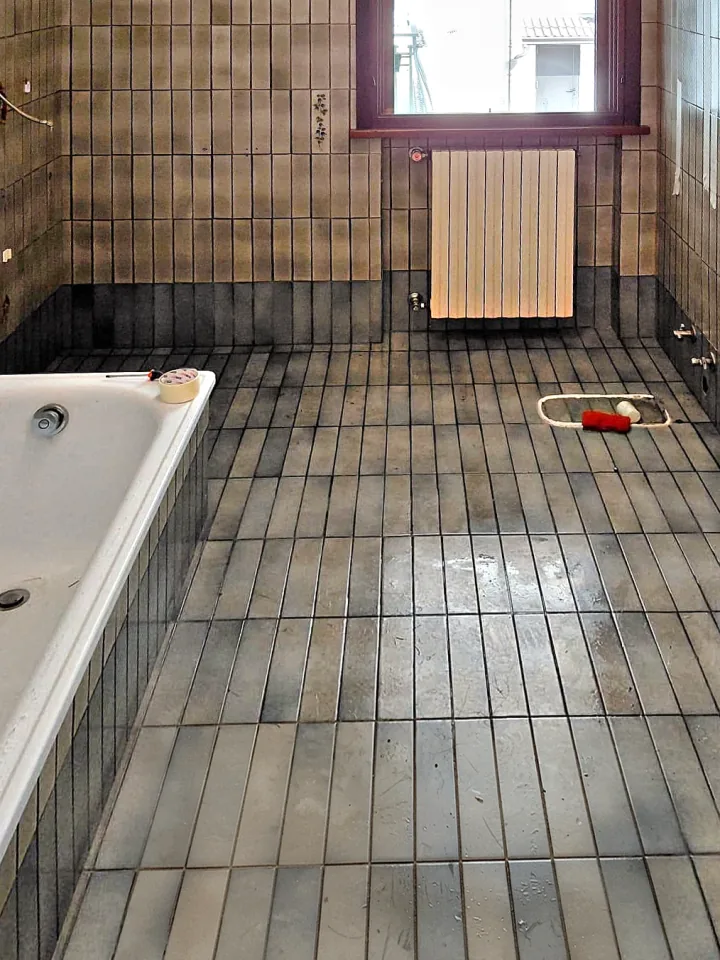 Prima: bagno con vasca, piastrelle scure a listelli e pavimento da rifare