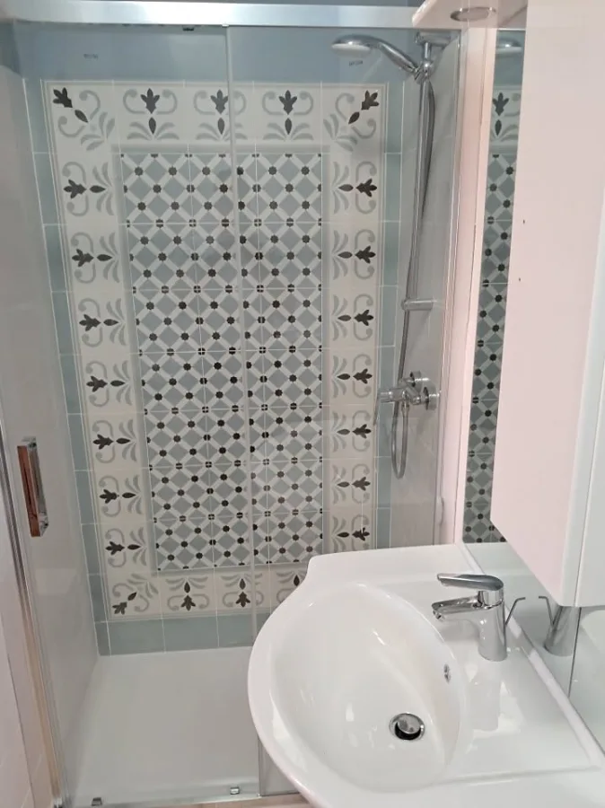 Doccia con rivestimento a decoro tipo cementina, box in vetro e lavabo